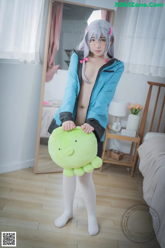 A woman in a blue jacket holding a green stuffed animal.