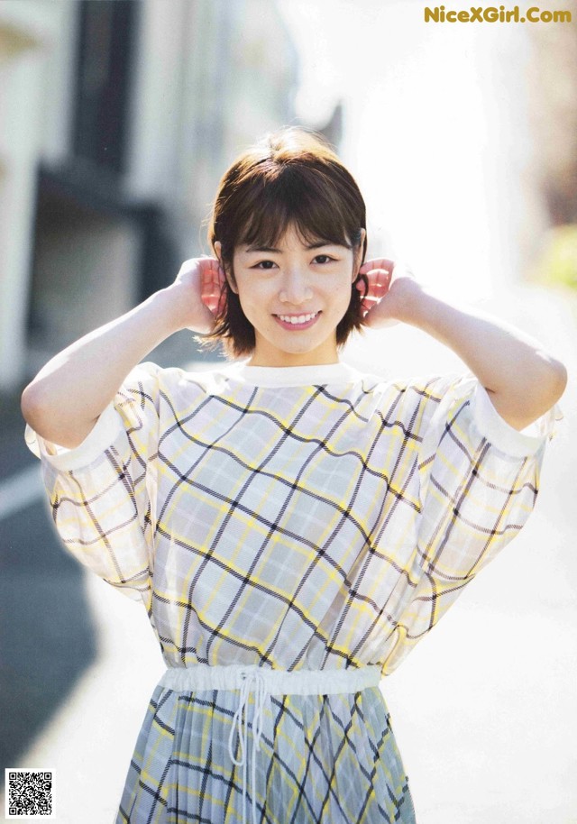 A woman in a yellow and white plaid dress posing for a picture.