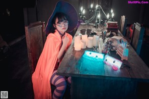 A little girl in a witches hat and glasses sitting at a table.