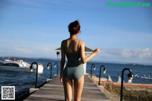 A woman in a black bathing suit standing on a rock by the ocean.