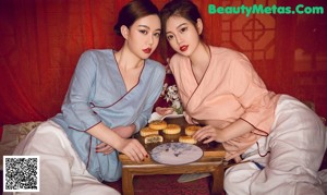 Two women sitting on a bed with a tray of food.