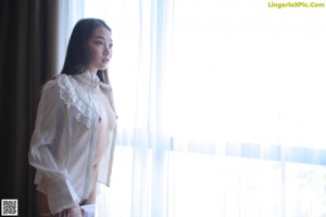 A woman in a white shirt and panties standing by a window.