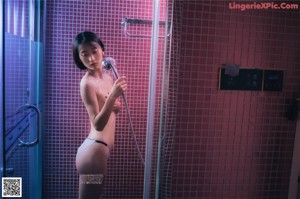 A naked woman standing in a bathroom next to a shower.