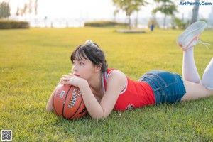 A woman sitting on the grass holding a basketball.