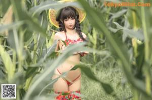 A woman in a red bikini and a straw hat standing in a field.