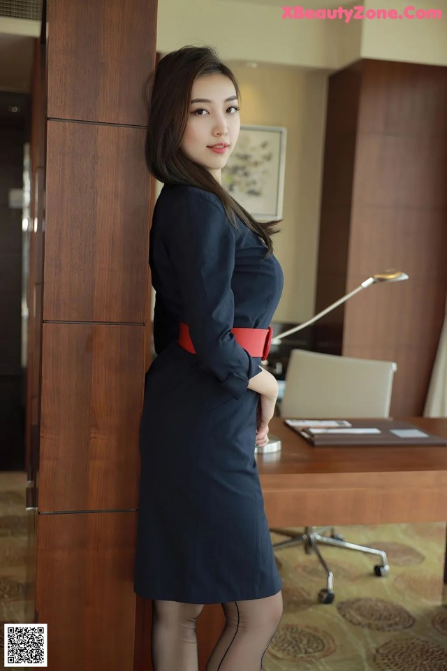 A woman in a blue dress standing next to a wooden cabinet.