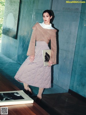 A woman standing in front of a desk holding a handbag.