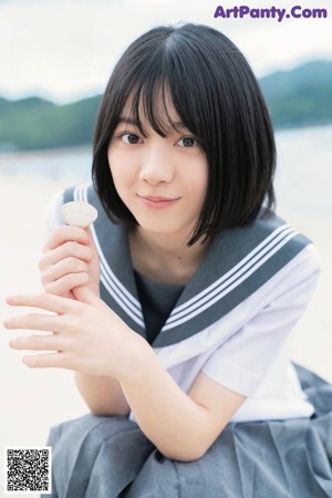 A young woman in a school uniform crouching on the beach.