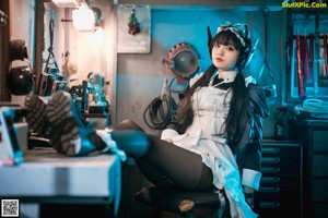 A woman in a maid outfit is sitting on a desk.