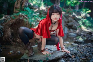 A woman in a red hooded outfit holding a basket in the woods.