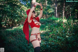 A woman in a red hooded outfit is posing in the woods.