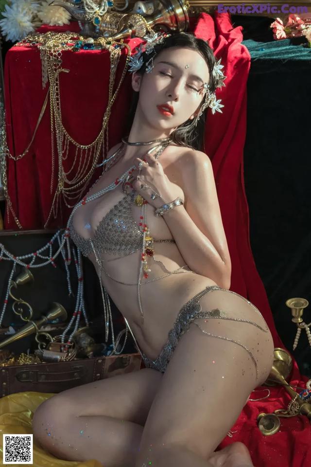 A woman in a silver bikini sitting on a red cloth.