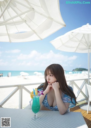A woman in a bikini sitting on the floor with her hand on her chin.