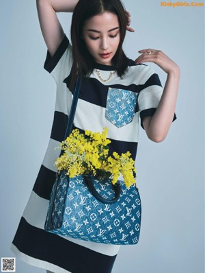 A woman in a black and white dress standing in front of a wall of paper flowers.