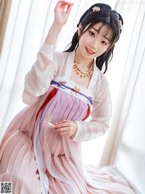 A woman in a pink and orange hanbok sitting on a couch.